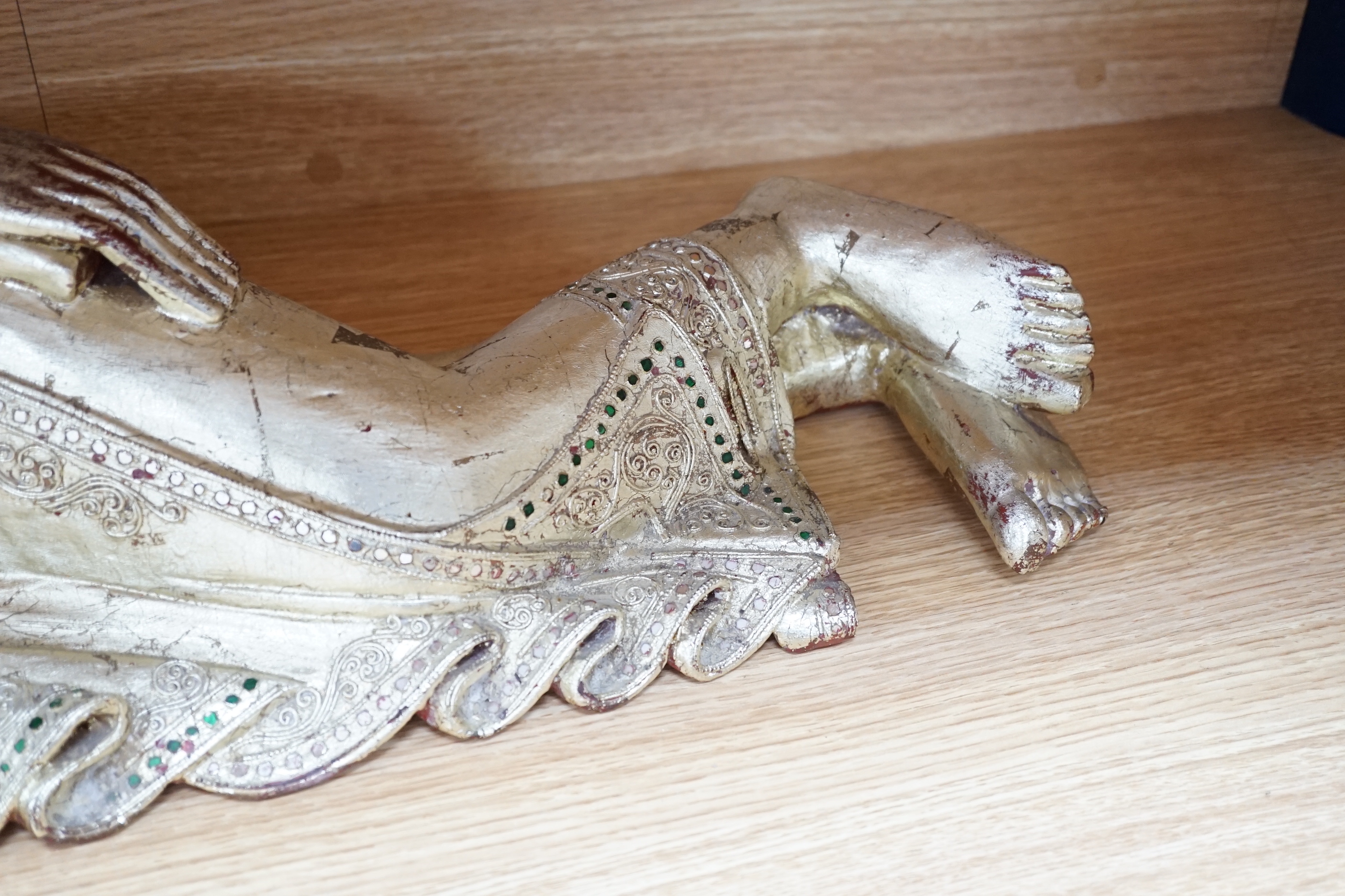 A 20th century Thai giltwood reclining figure with inset coloured glass decoration, 78cm long
